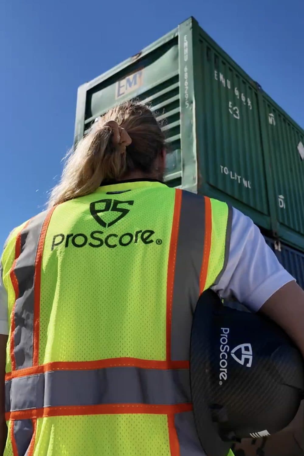 A ProScore crew member in a hi-vis vest carrying a hard hat on a work site