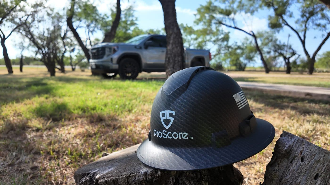 A ProScore-branded hard hat resting on a stump with a work truck and open land behind it in golden daylight