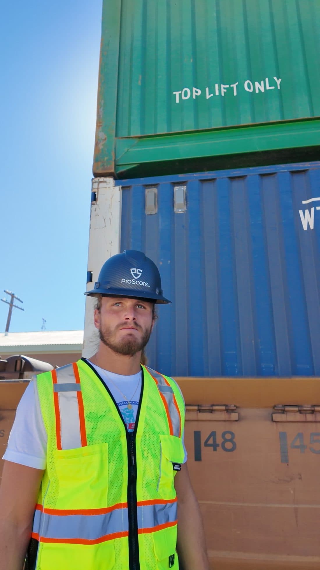 A ProScore worker in a hard hat and hi-vis vest standing in front of shipping containers on a project site