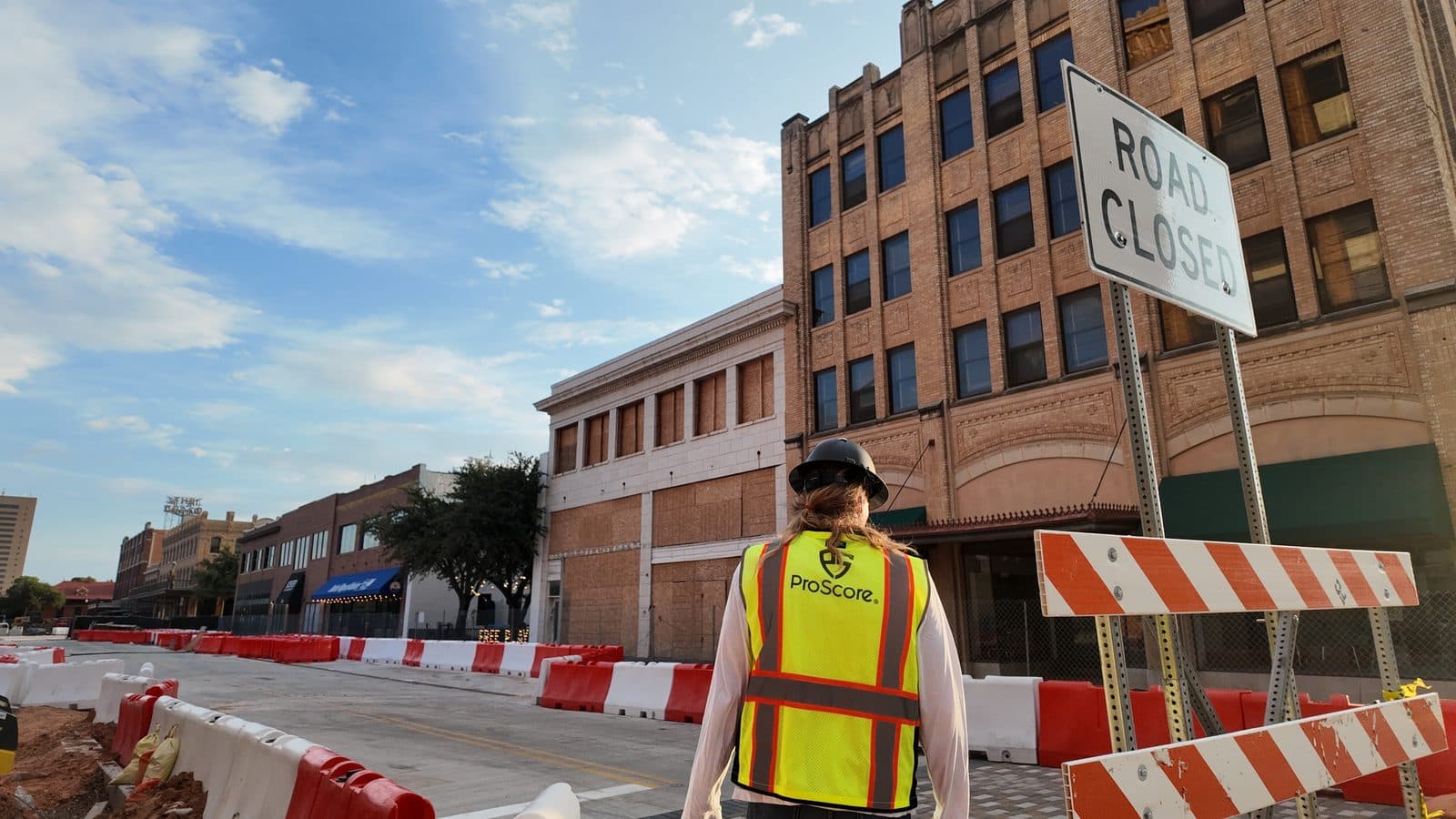 A worker in a ProScore hi-vis vest performing daylight street infrastructure work near road-closed signage